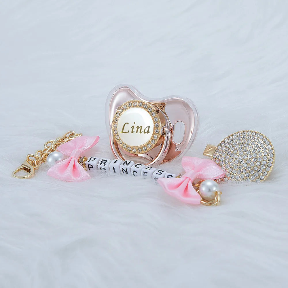 A pink crystal pacifier with a clip featuring the name Lina and matching pink ribbon and pearl accents.