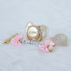 A personalized crystal pacifier featuring a name, set with matching clip and pearl accents.