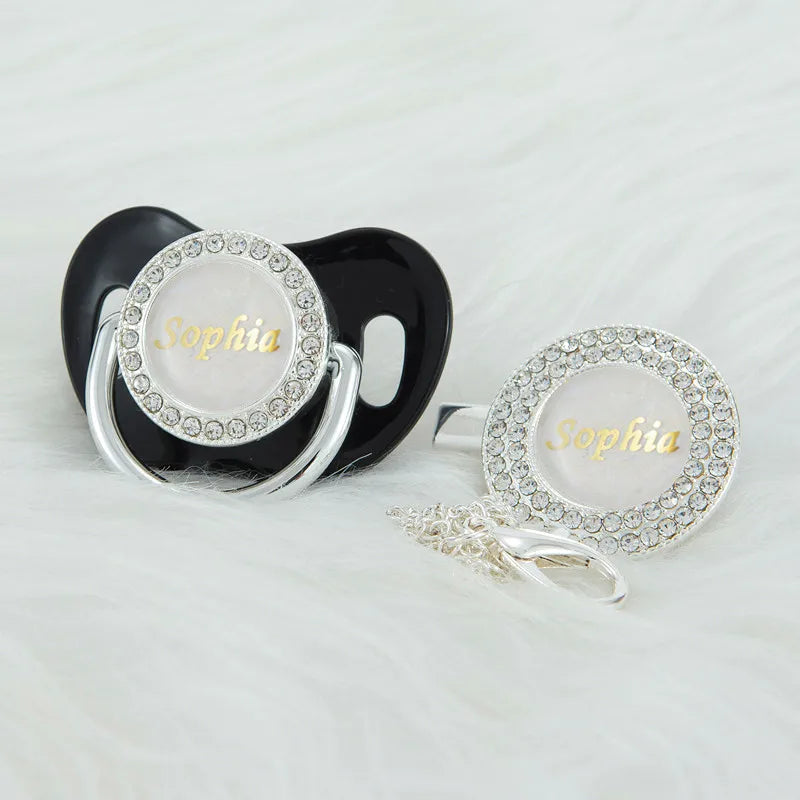 A black silicone pacifier clip with a white rhinestone nameplate spelling Sophia
