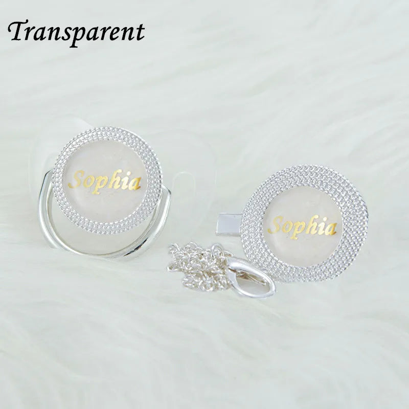 A set of transparent rhinestone pacifiers and clips with the name Sophia engraved on them.
