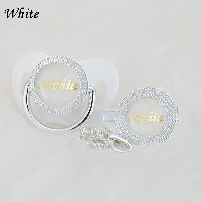 A set of white rhinestone pacifiers and clips with the name Sophia engraved on them